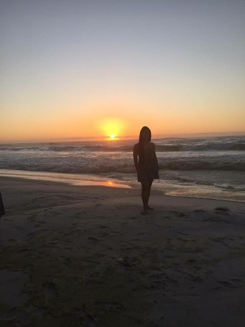 A person posing on the beach with a sunset in the background.
