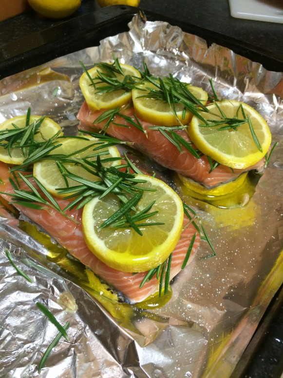 Raw salmon pieces topped with herbs and lemon slices on top of tin foil.