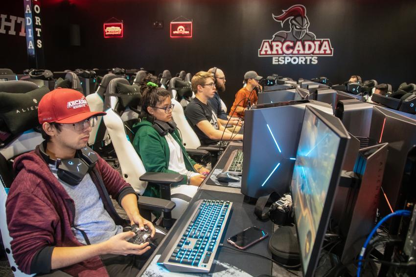 Five students at computers with the Arcadia esports logo to the right side.