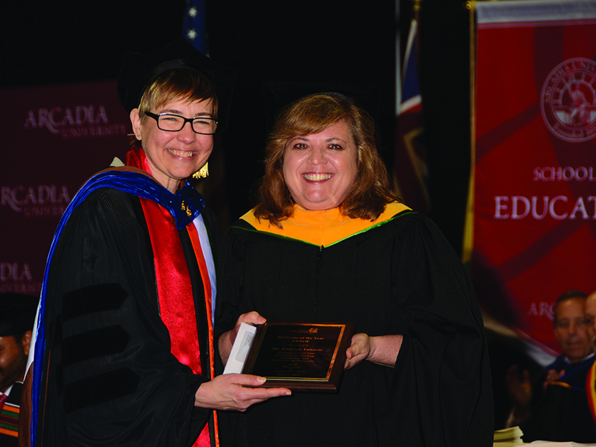 Kathy Valverde holding her award and smiling into the camera with another faculty member.