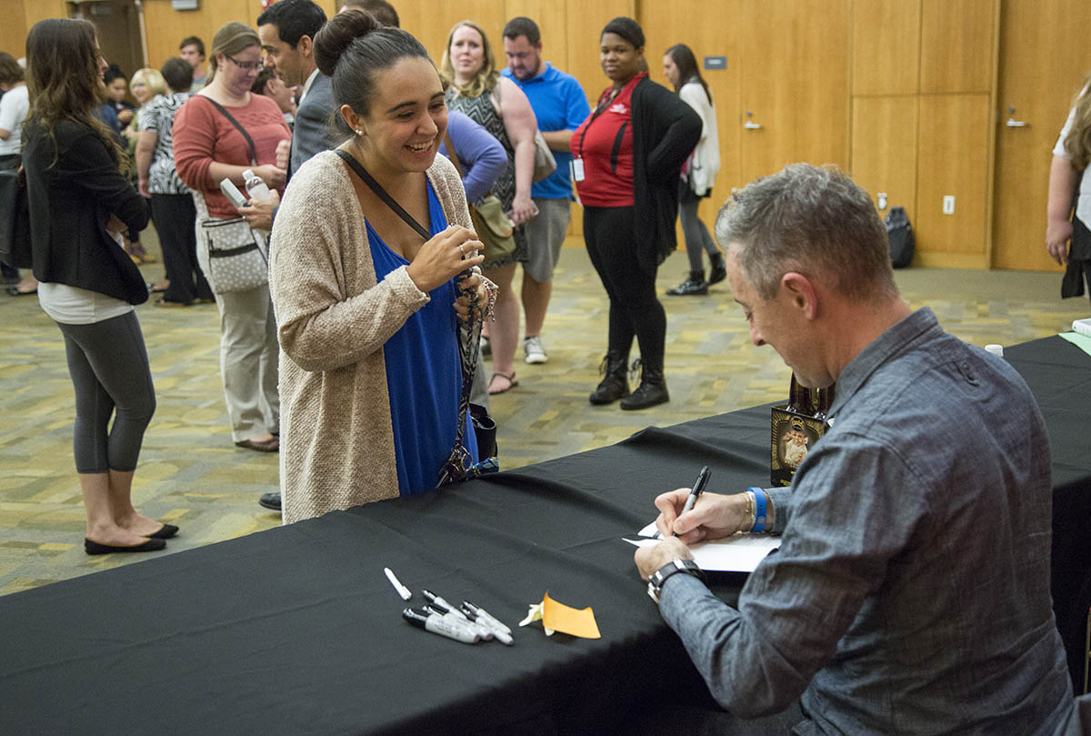 A person smiling as Alan Cumming signs their book.