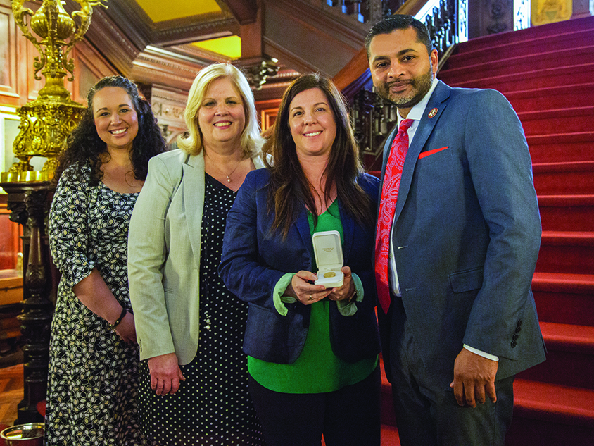 Heather Mazzanti McKiernan holding an award in her hands and posing with others including President Nair.