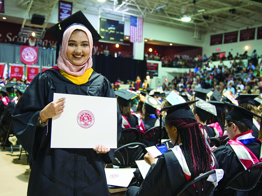 A graduating woman in regalia holding her diploma envelope.