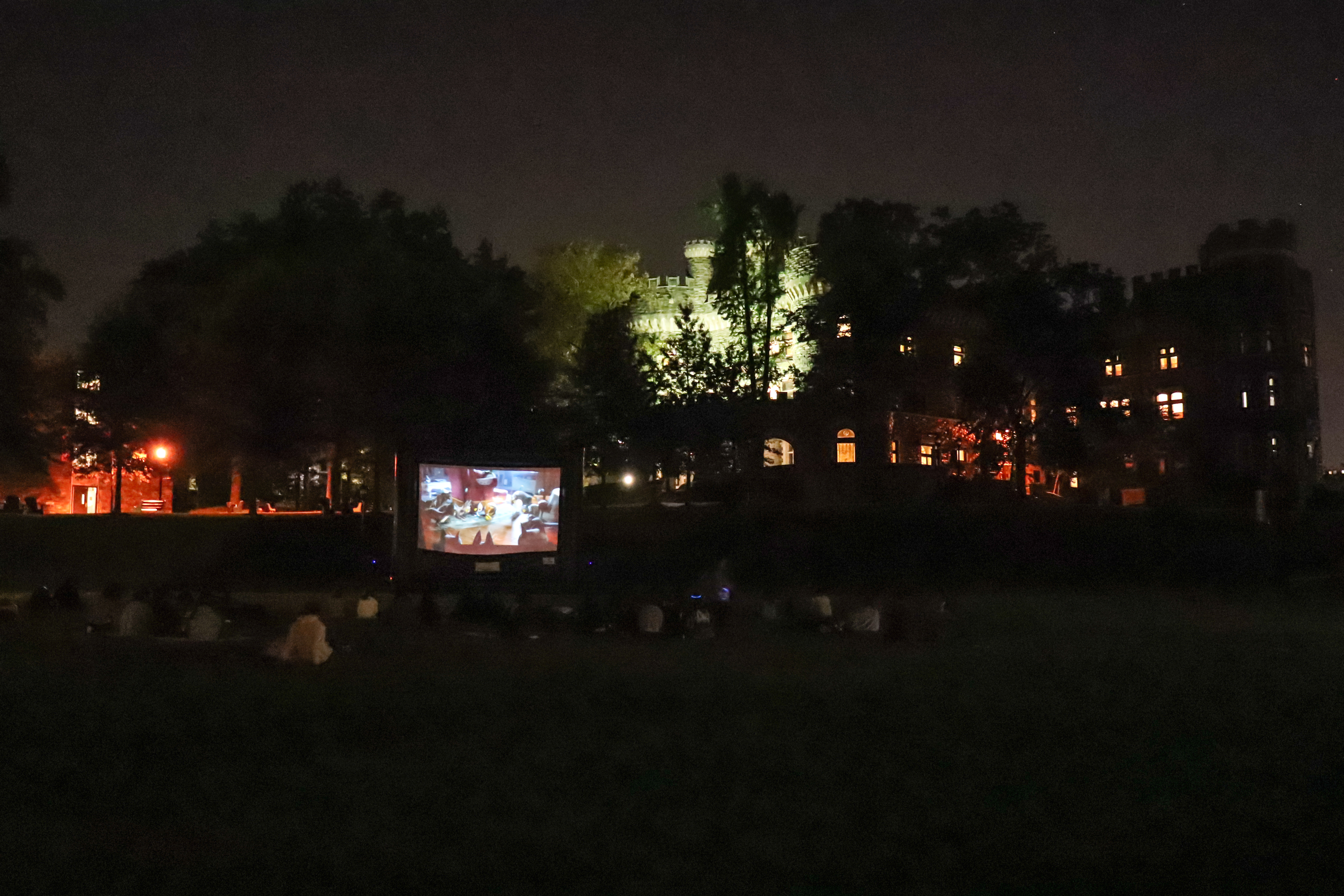 Students watching a film on a projected screen outside under the stars.