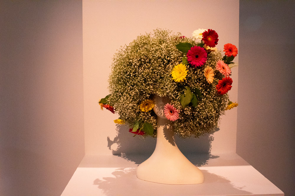 White mannequin head with an afro created from plants and flowers.