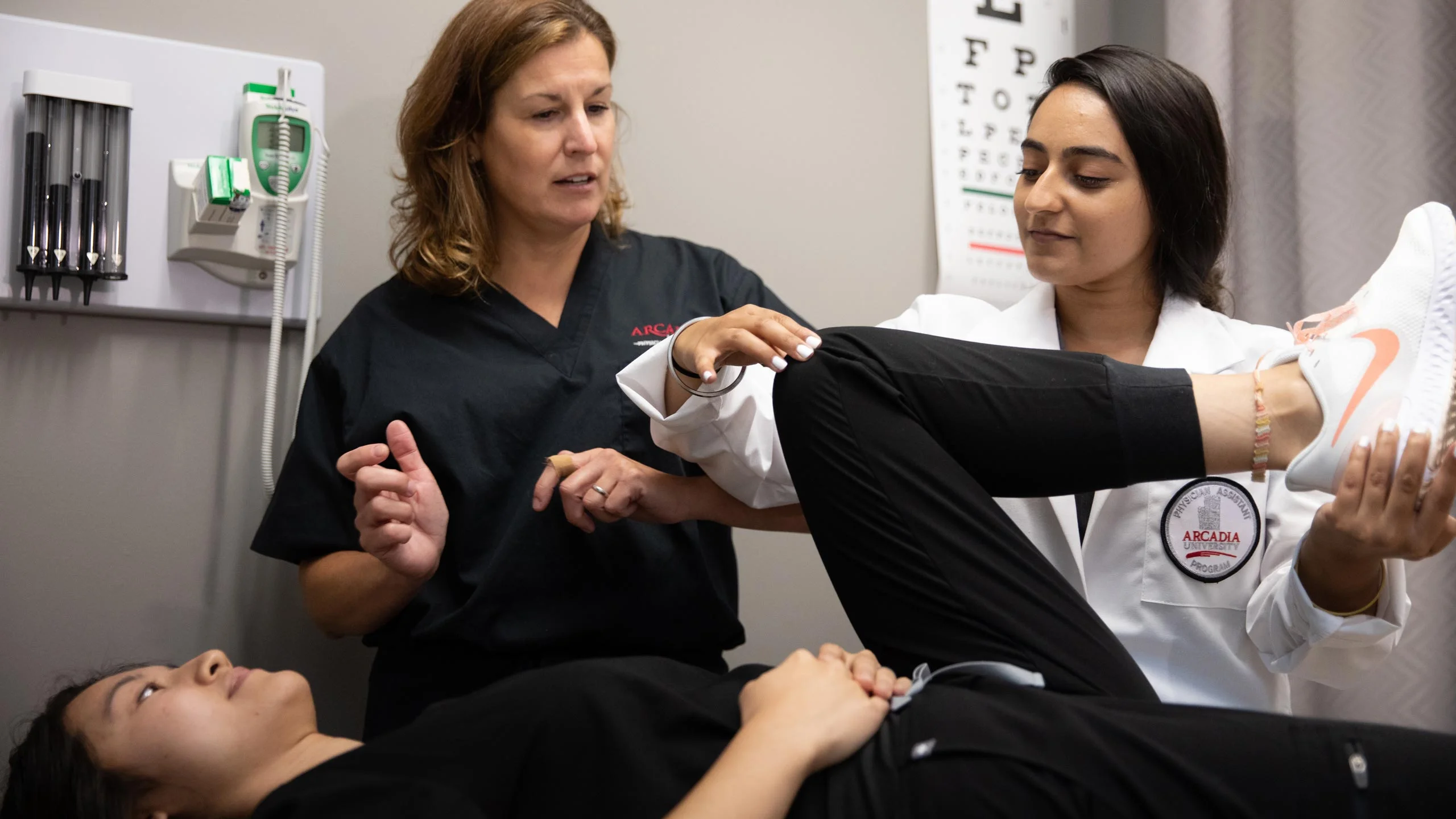 A physician assistant student conducts an examination while a professor provides instruction.