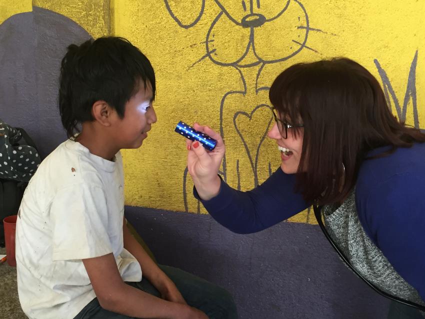 A woman with a stethoscope around her neck shines a light into the eyes of a smiling boy