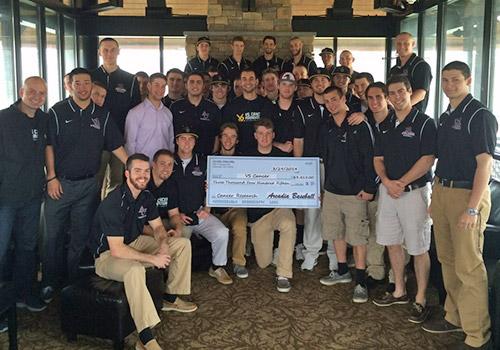 A large group of young men stand and sit around a large donation check