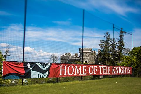 Home of the Knights banner on a fence with Grey Castle in the background