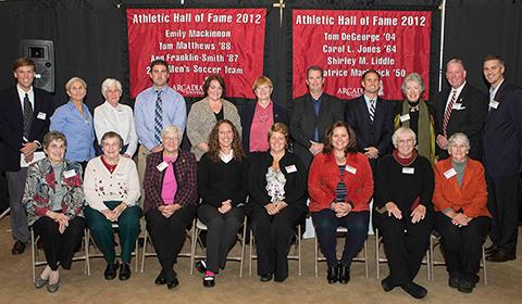 Members of the athletic hall of fame sitting in front of two banners