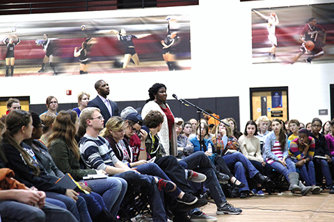 Students sitting listening to speech as others ask questions at a mic.