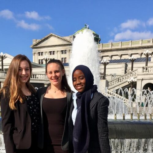 Three female students standing in front of a fountain.