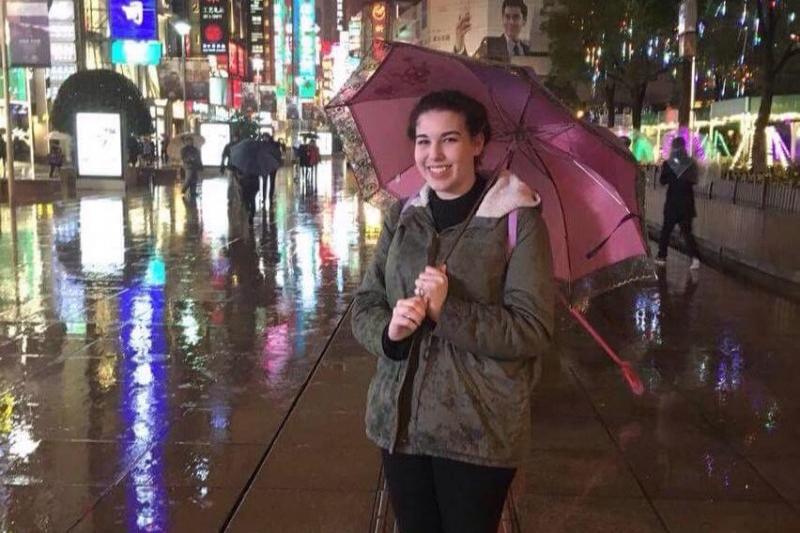 Student stands with umbrella on a busy street in China at night.