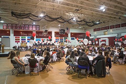 A wide shot of the interior of the Alumni Gym, which is filled with round tables with red and black and white balloon centerpieces at which people are seated