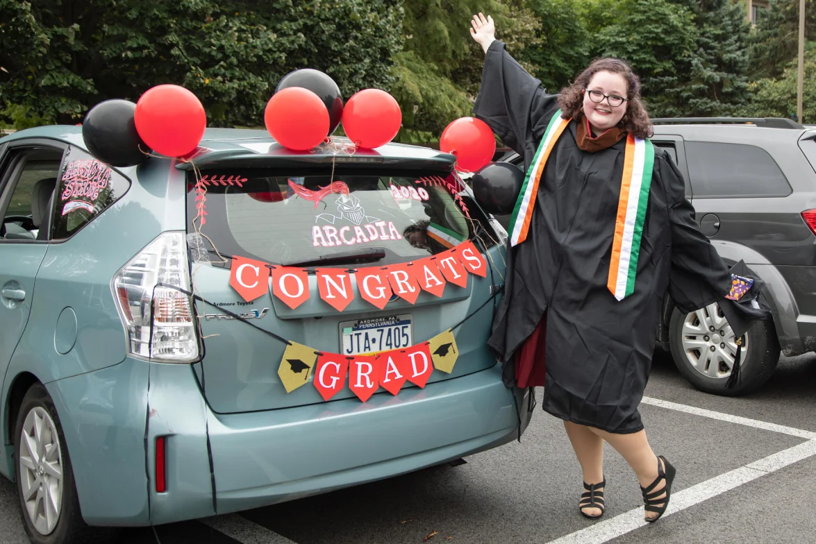 A graduating student posing with her car that has a banner saying "Congrats Grad"