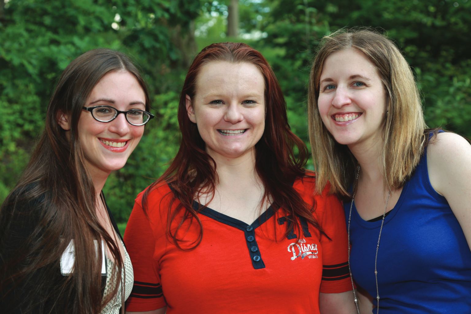 Three young female alumni smile at camera