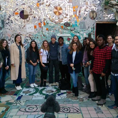 A group of Arcadia University Students standing together and smiling at the camera in front of a mosaic that spans across the walls and floor.