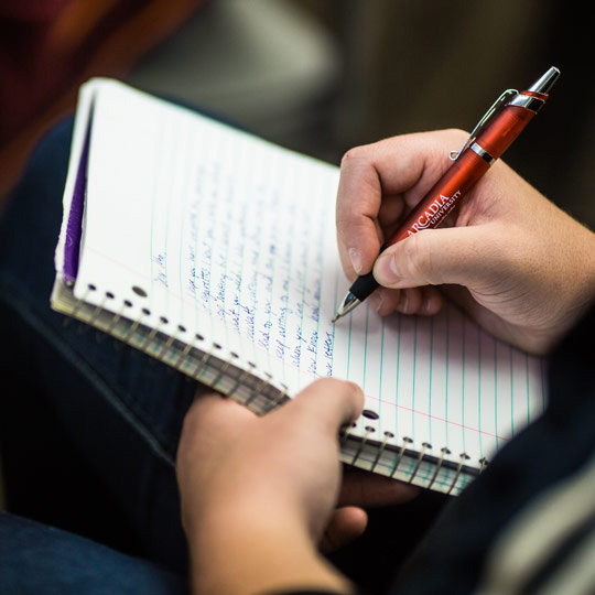 Student writes by hand into a spiral notebook with a pen.