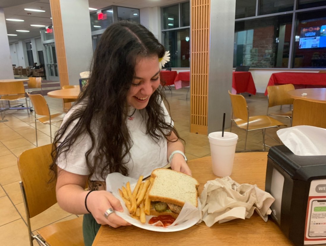 A student smiling while looking at her sandwich and french fries