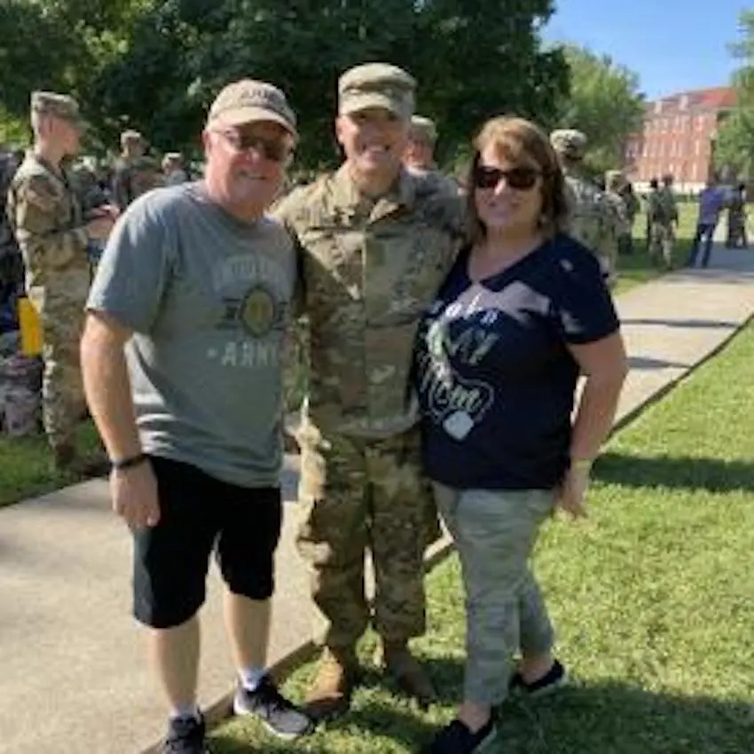 Dean Cahill ’22, Biology major wears Army fatigues and stands with his parents outside.