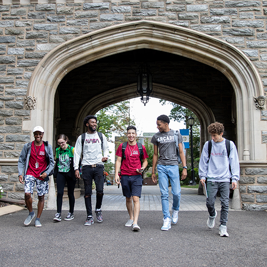 Six students walk through the former stone gateway on campus.