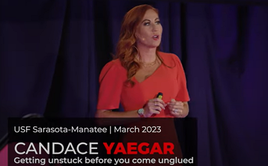 Candace Yaeger '07 on stage during her TEDx debut. She is using a microphone and wearing a red dress.