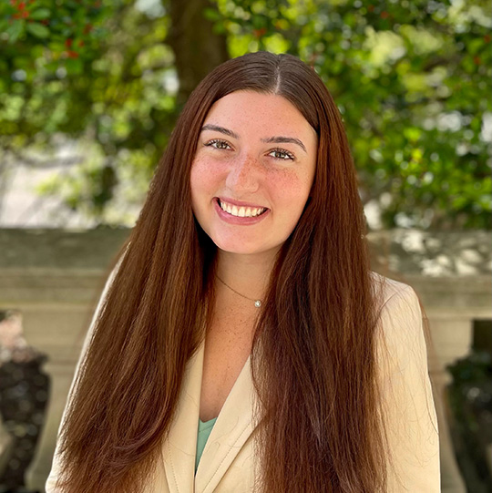 Allannah Giles Coordinator of Student Engagement smiles in front of a green tree on campus.