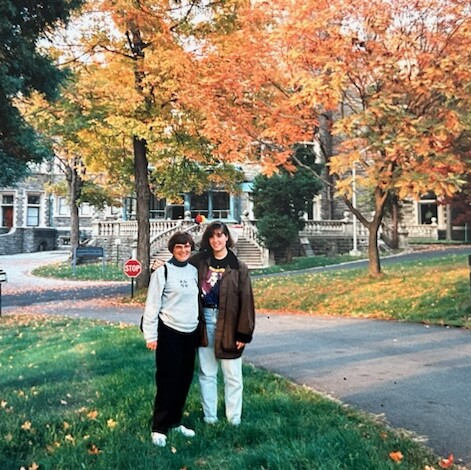 Winnifred and Sally are standing on campus with trees and the Grey Towers Castle behind them.