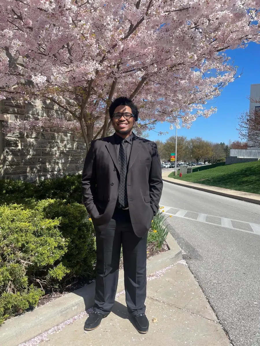 Oshane Mendez '24 wearing a suit and standing in front of a flowering tree
