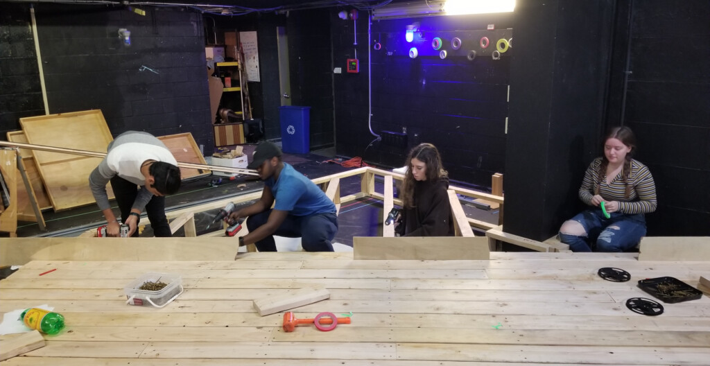 Four people working together to create a wooden platform