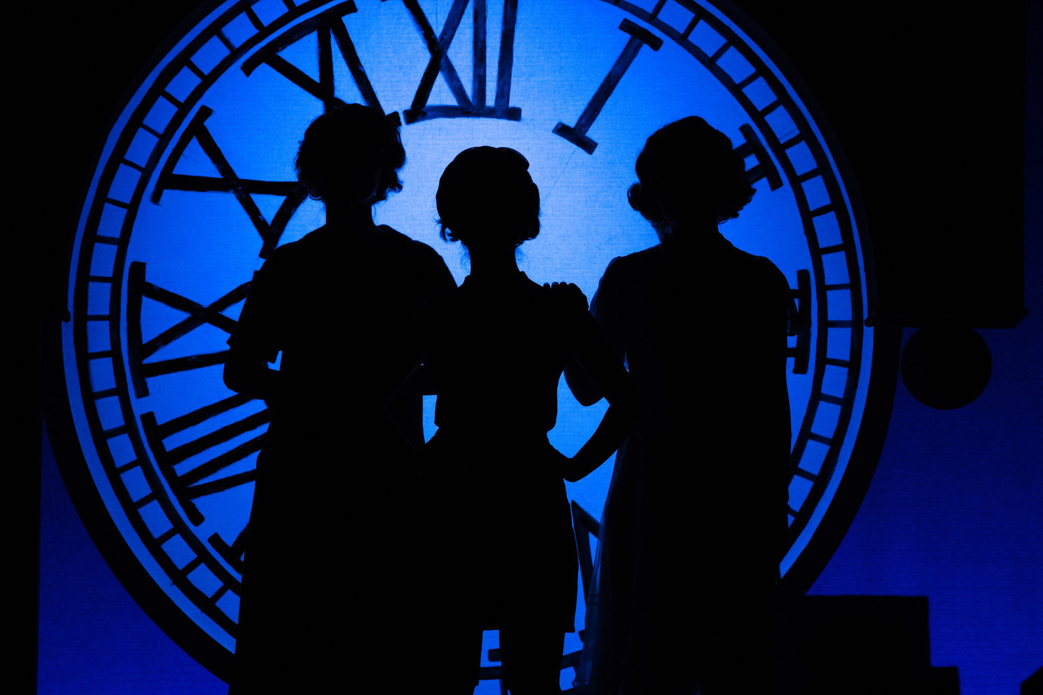 Three silhouettes of people on stage with a blue background and clock tower