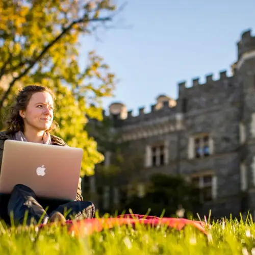 female students sitting in front of The Csatle on her laptop