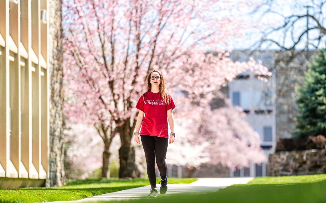Student walking across campus in the spring. flower tree is blooming behind them.