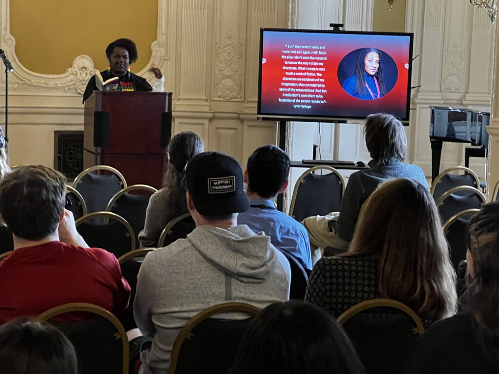 A Black woman reading a book to an audience