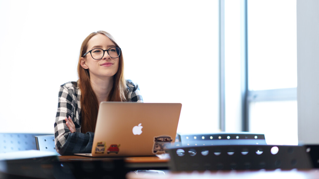 A student leans against her computer and grins during a lecture in a creative writing class.