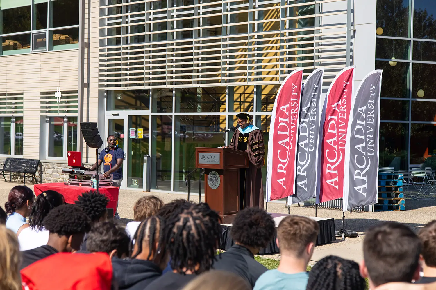 Dr. McCargo speaking at the podium during Convocation, wearing a student's pair of sunglasses.