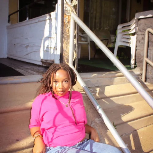 Fatoumata Sidibe sitting on porch steps with chairs behind her.