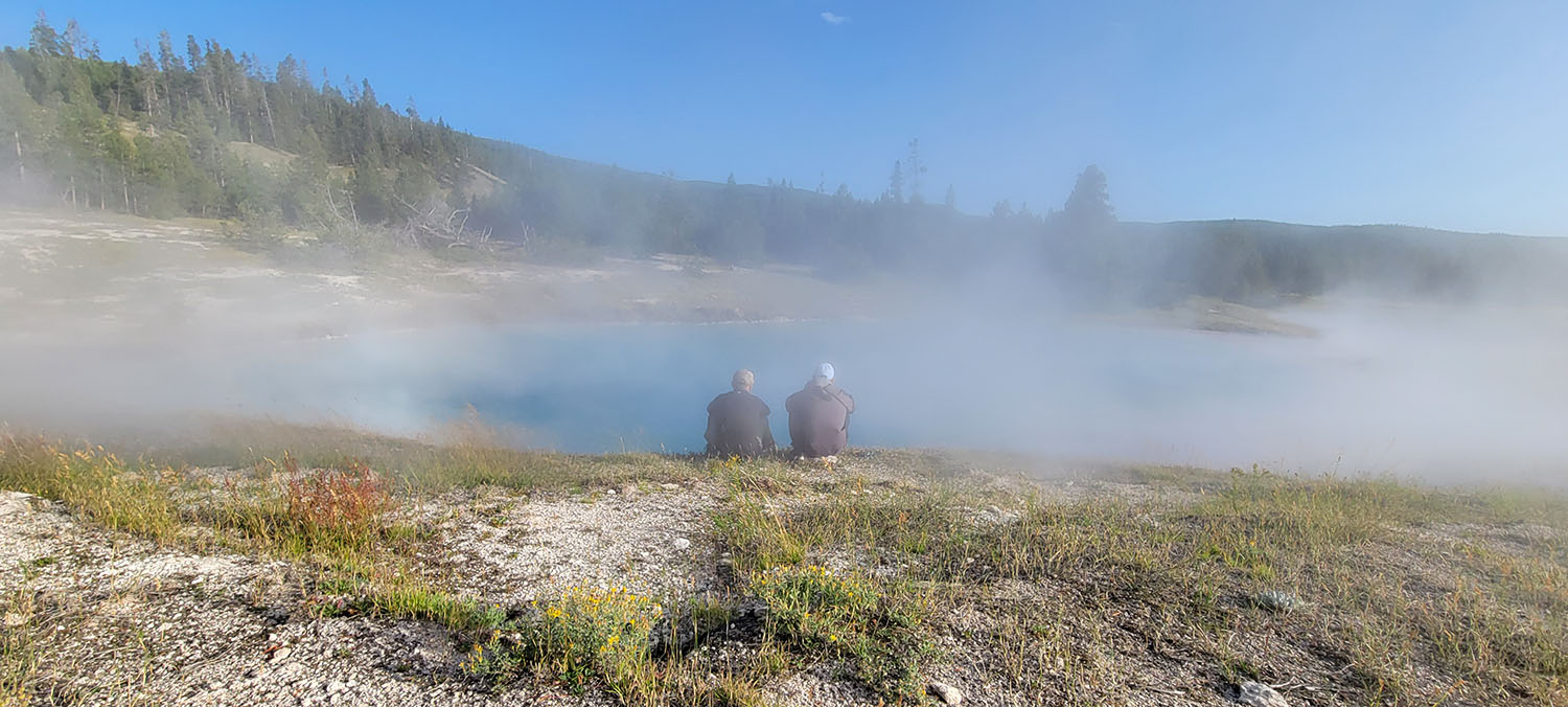 Two people sitting in front of a lake in Yellowstone National Park.