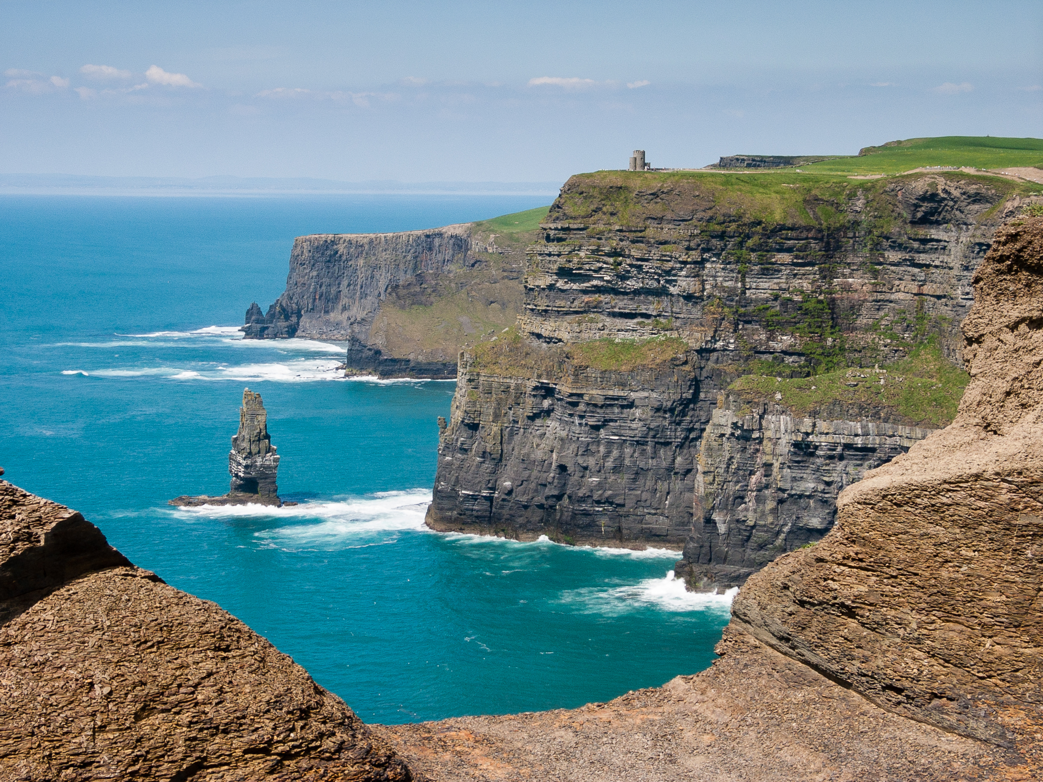 Cliffs of Mohor - green and stone cliffs off coast of Ireland with bright blue water on a sunny day