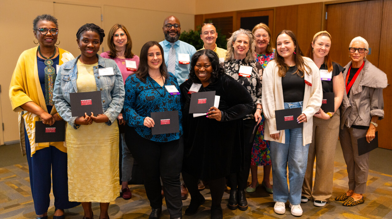 A group of people smiling into the camera and holding black folder with Knights