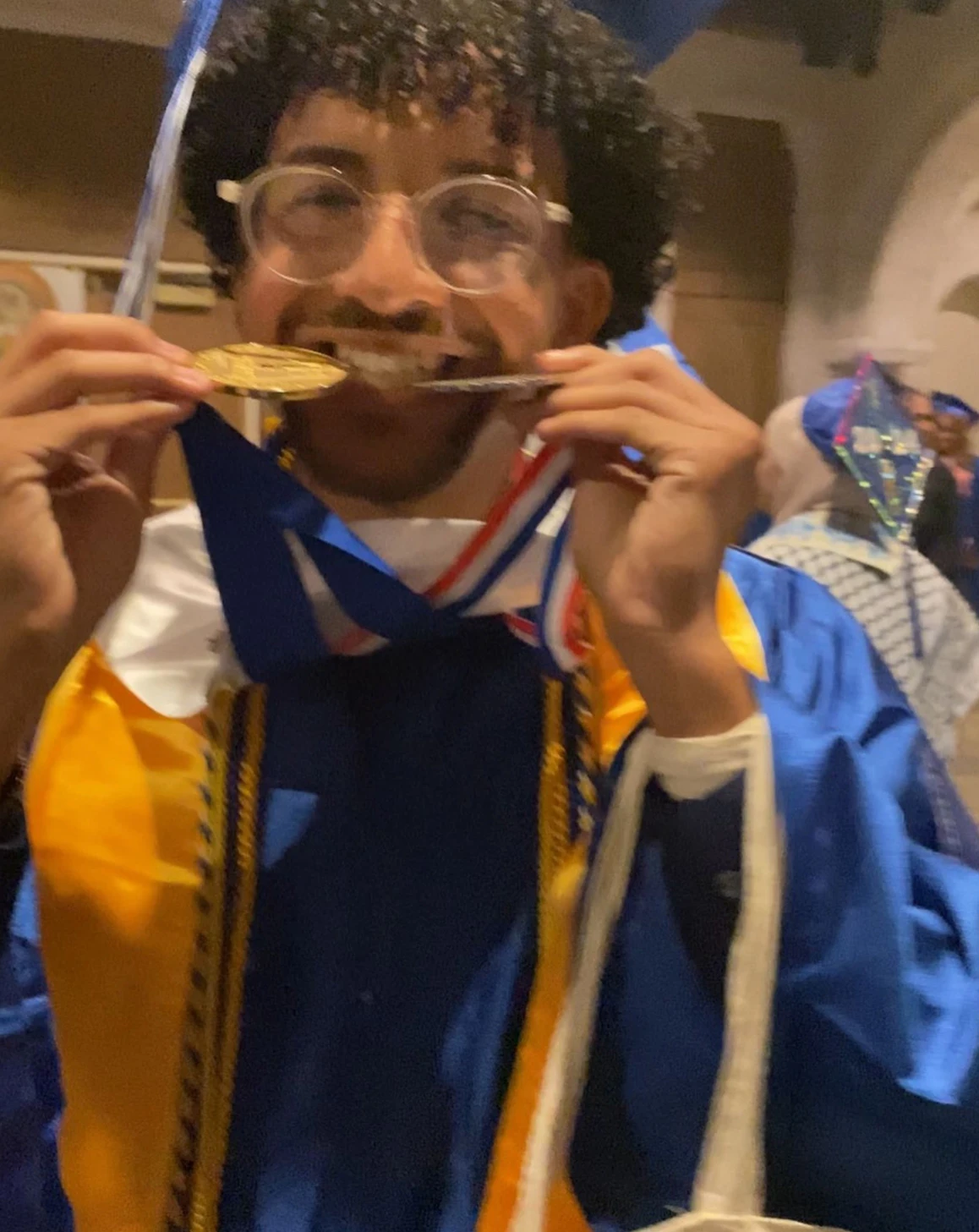 Ian Catalino-Vasquez ’28 biting gold medals in his high school graduation regalia.