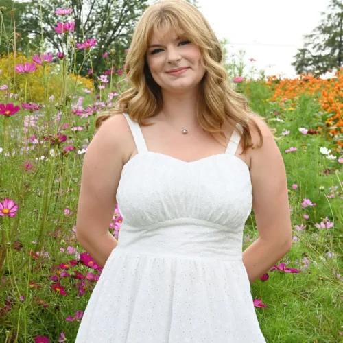 Kylee Kramer in a white dress posing with a field of flowers behind her.