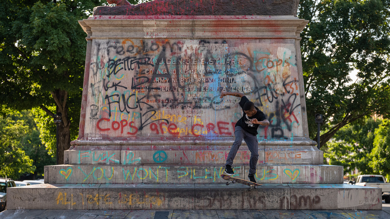 Young black man skateboarding on monument of JEB Stuart covered with grafitti.