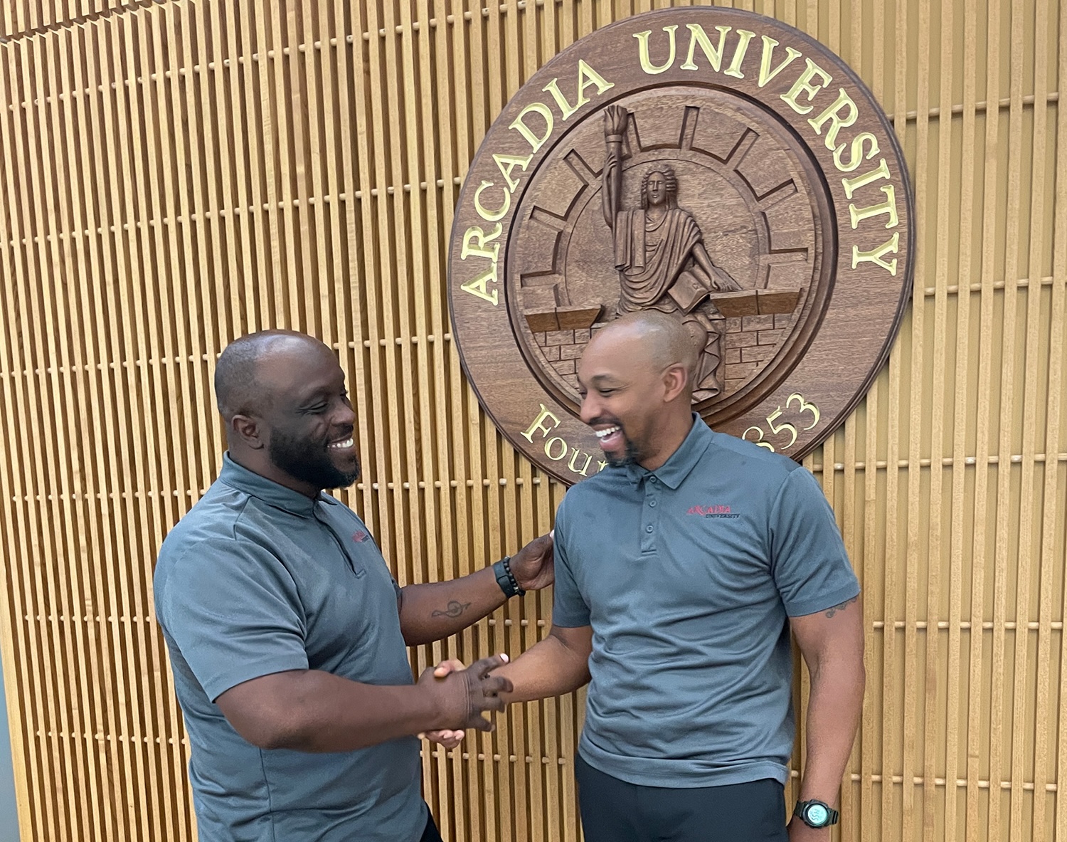 Eugene Garmon (left) and Dr. Donavan McCargo (right) shaking hands in front of the Arcadia University seal.