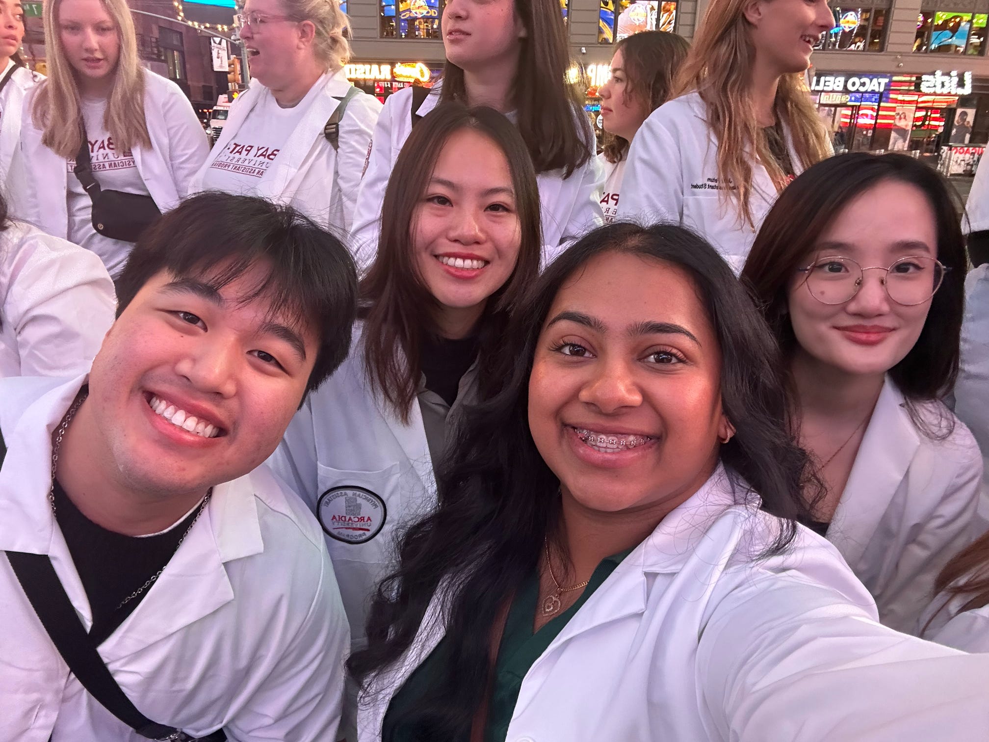 A group of PA students from the Class of 2026 take a selfie wearing their white coats