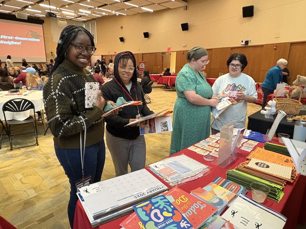 students hold up planners they picked up at wellness services' table at the first-generation college student celebration in the great room