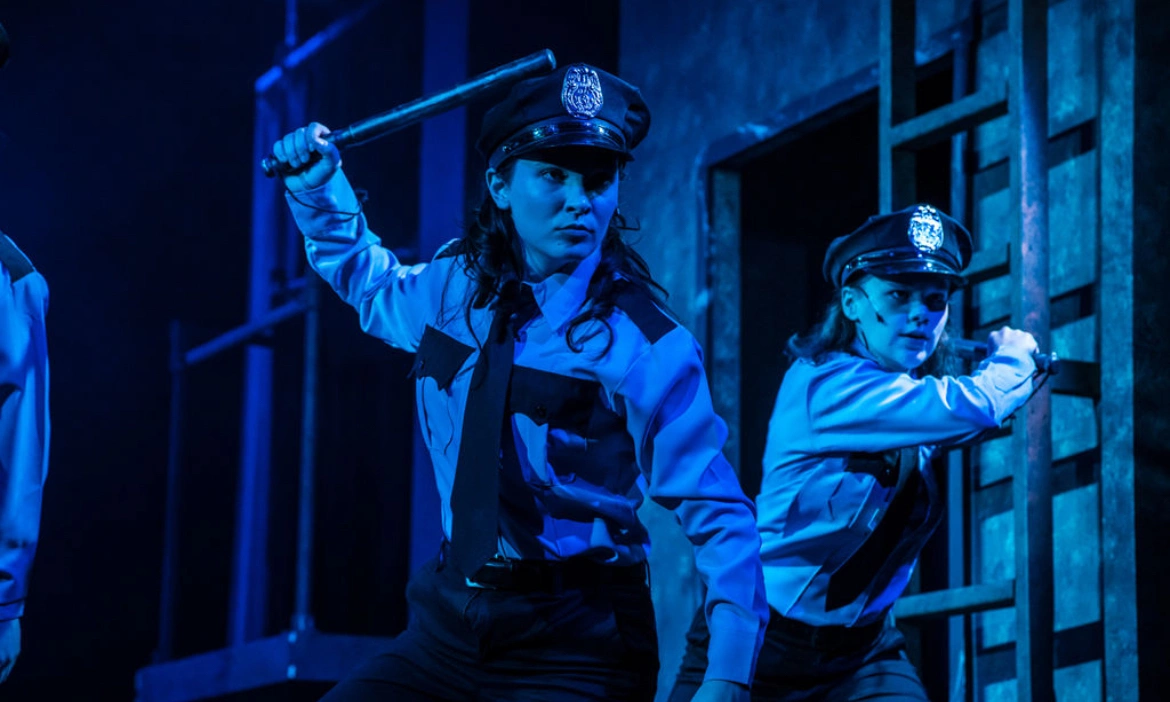 Two actors in police wardrobe holding a baton for a play production.