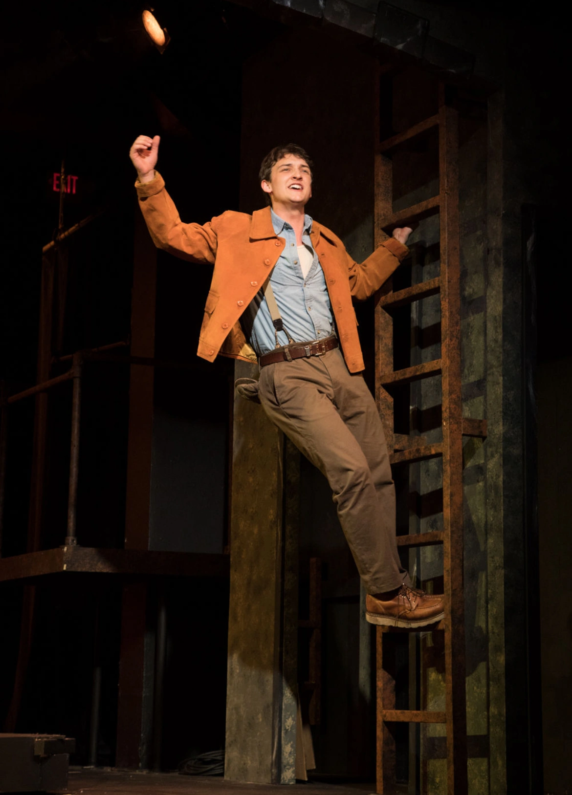 An actor on a ladder and singing in a play production.