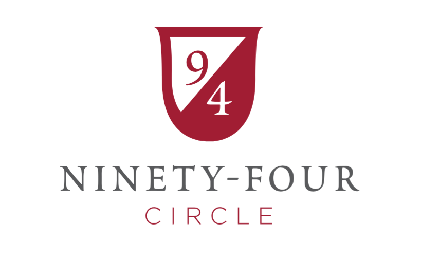 University Advancements 94 Circle logo has a shield in white and a burgandy red color.