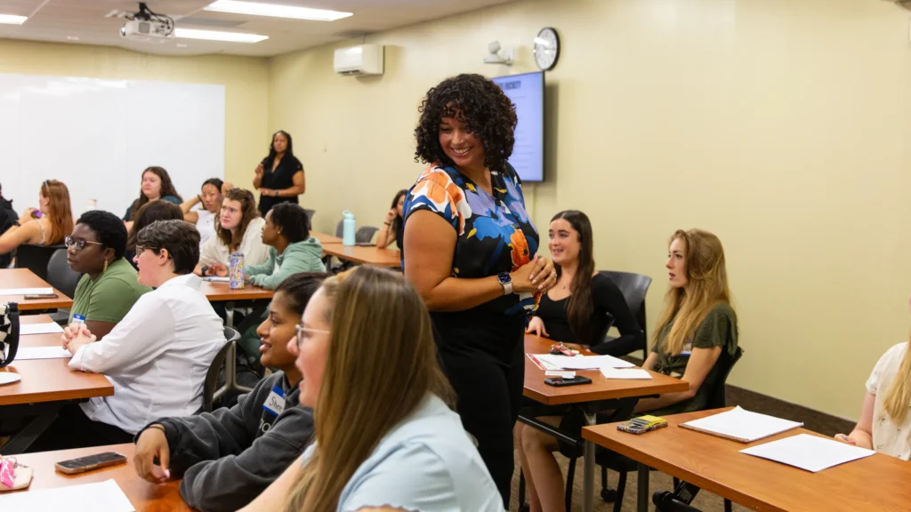 A professor walks around the classroom speaking to Counseling students at their graduate orientation.